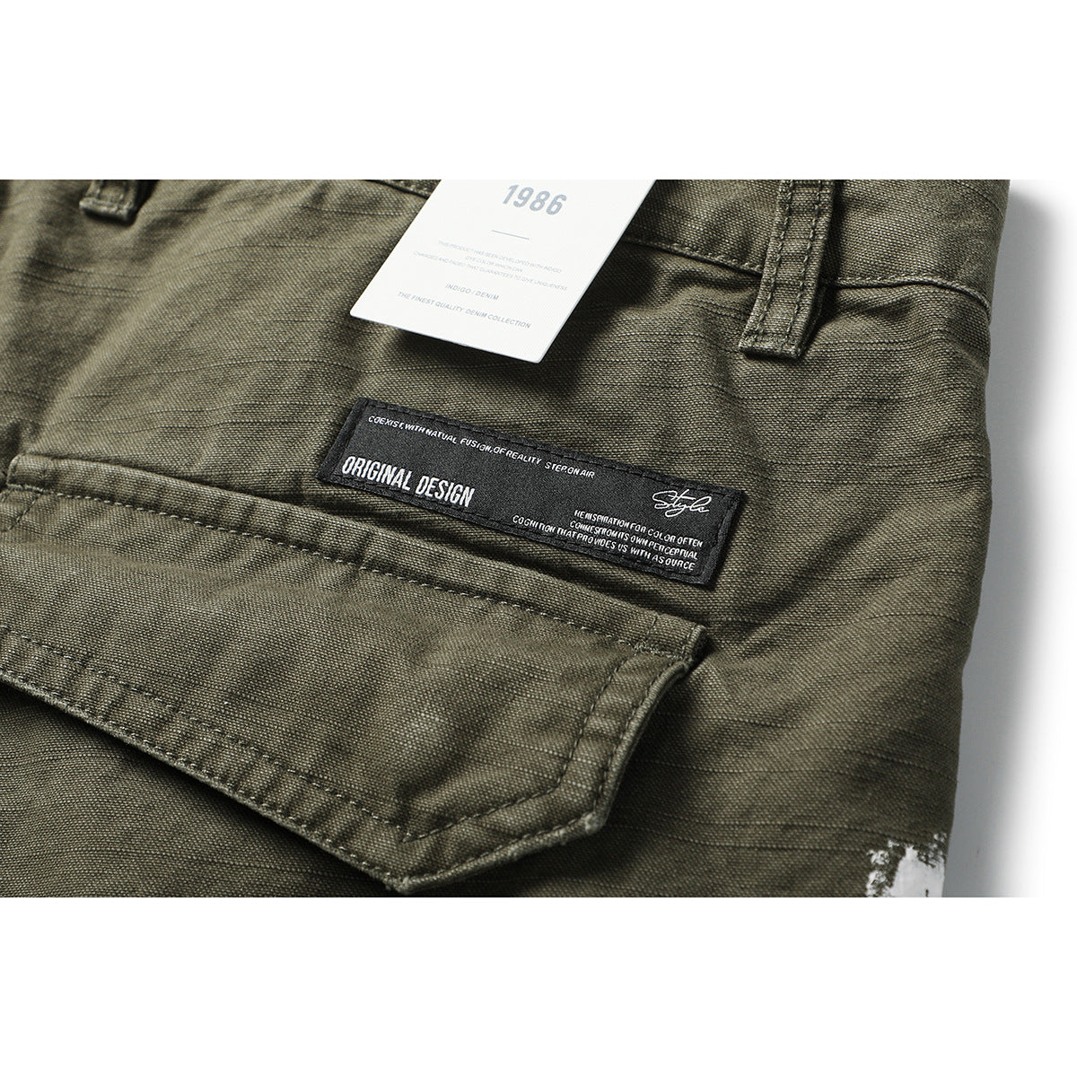 Close-up of olive cargo shorts showing a pocket, waistband loop, and attached English-language tags.