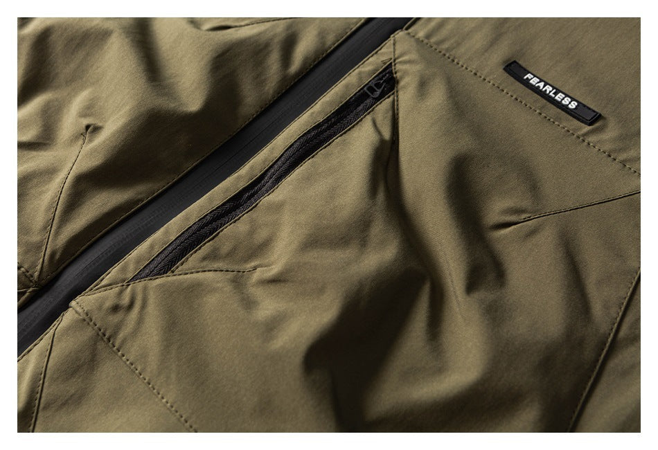 Close-up of an olive jacket pocket, diagonal black zipper, stitched seams, and a FEARLESS fabric badge.