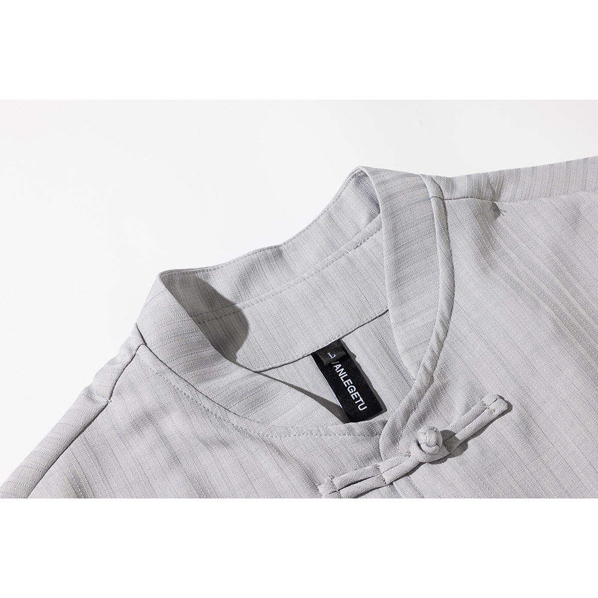 Close-up of a light gray striped shirt collar, inner neck label, and frog-style closure.