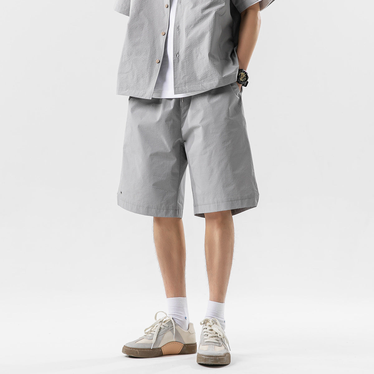 Front view of a model wearing light gray knee-length shorts with a matching button-front shirt.