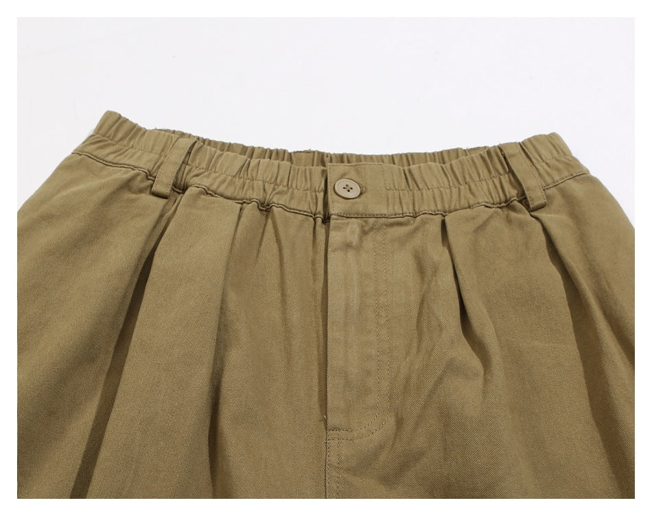 Close-up of khaki pants showing the elastic waistband, button closure, belt loops, pleats, and front fly.