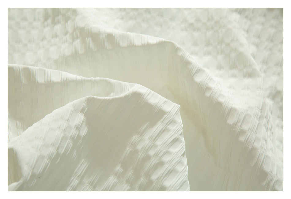 Close-up of off-white fabric arranged in soft folds, showing a subtle woven texture.