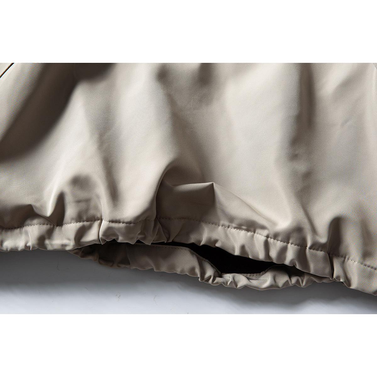 Close-up of a light taupe jacket’s gathered elastic hem and stitched seam.