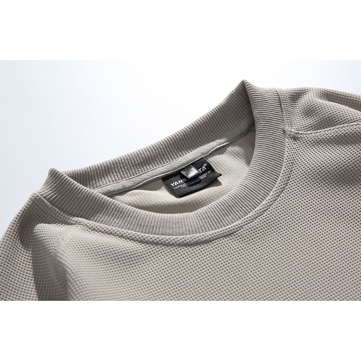 Close-up of a light gray waffle-textured sweatshirt neckline with a ribbed crew collar and sewn-in label.
