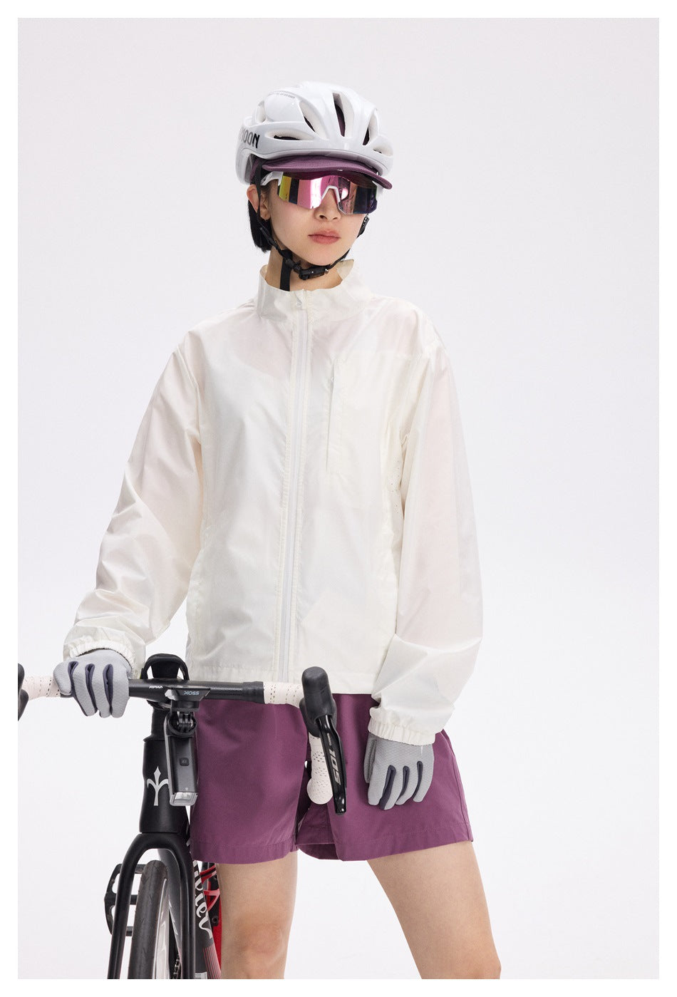 Cyclist wearing a white zip-front jacket and plum shorts, shown from helmet to mid-thigh with a bike.