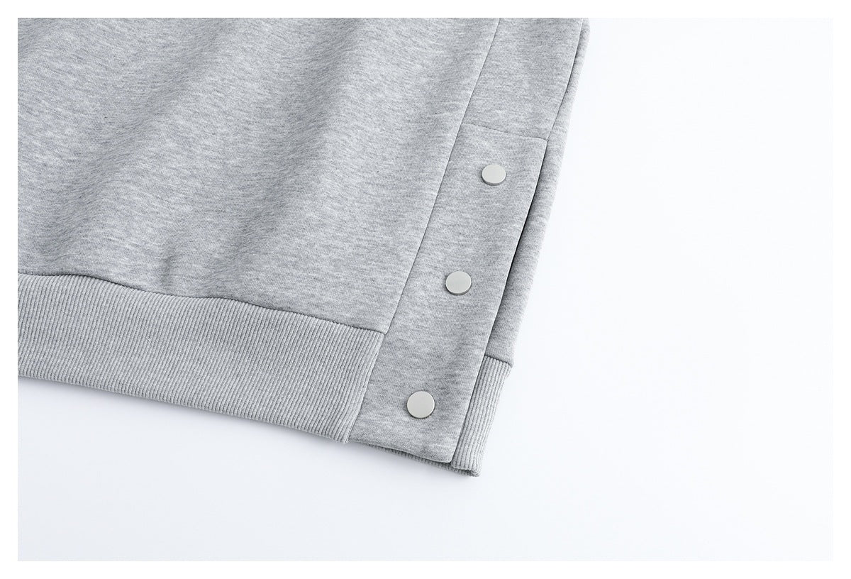 Close-up of the light gray sweatshirt hem with three round snap fasteners along the side.