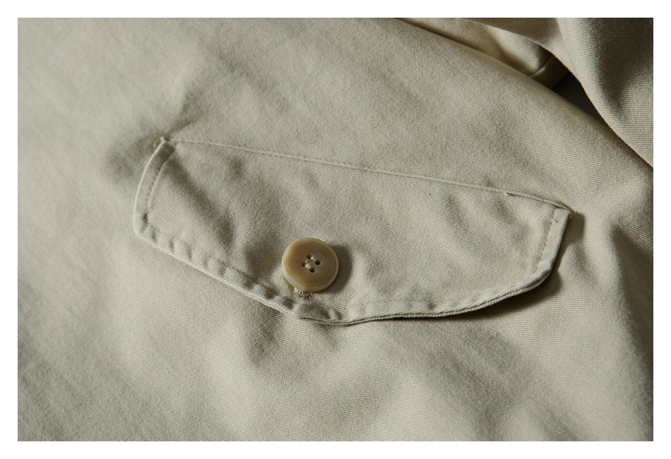 Close-up of a light beige jacket's buttoned pocket flap and stitching.