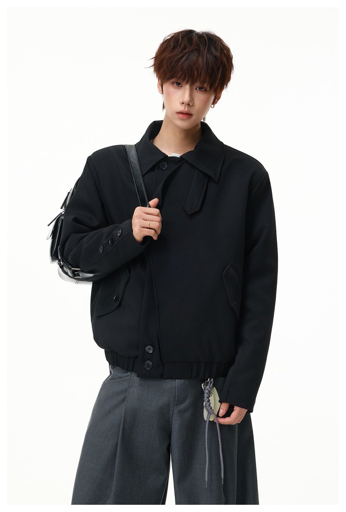 Model wearing a black jacket with a wide collar, angled button front, and flap pockets; shown from the waist up.