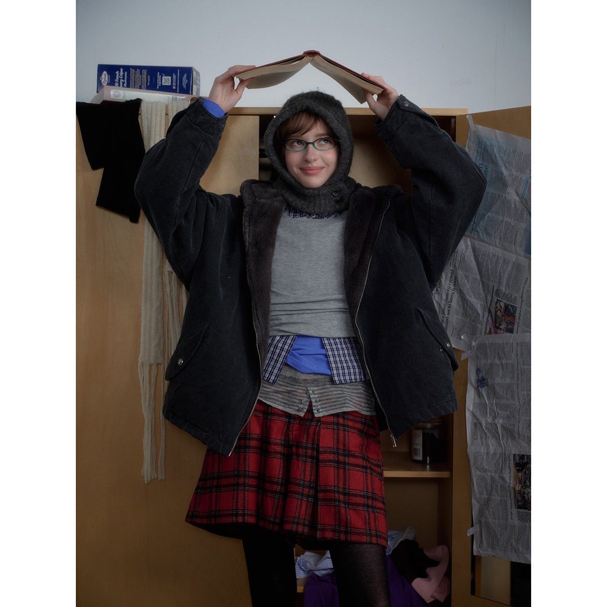 Front view of a person in a charcoal hooded jacket with dark plush lining, layered over a gray top and red plaid skirt.