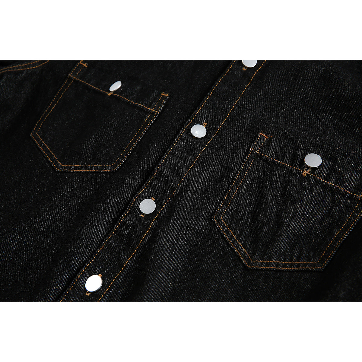 Close-up of a black denim shirt front with two patch pockets, silver snaps, and orange stitching.