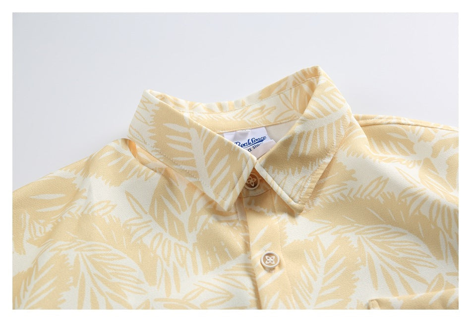 Close-up of a pale yellow tropical leaf-print shirt showing its pointed collar, buttons, and inner neck label.