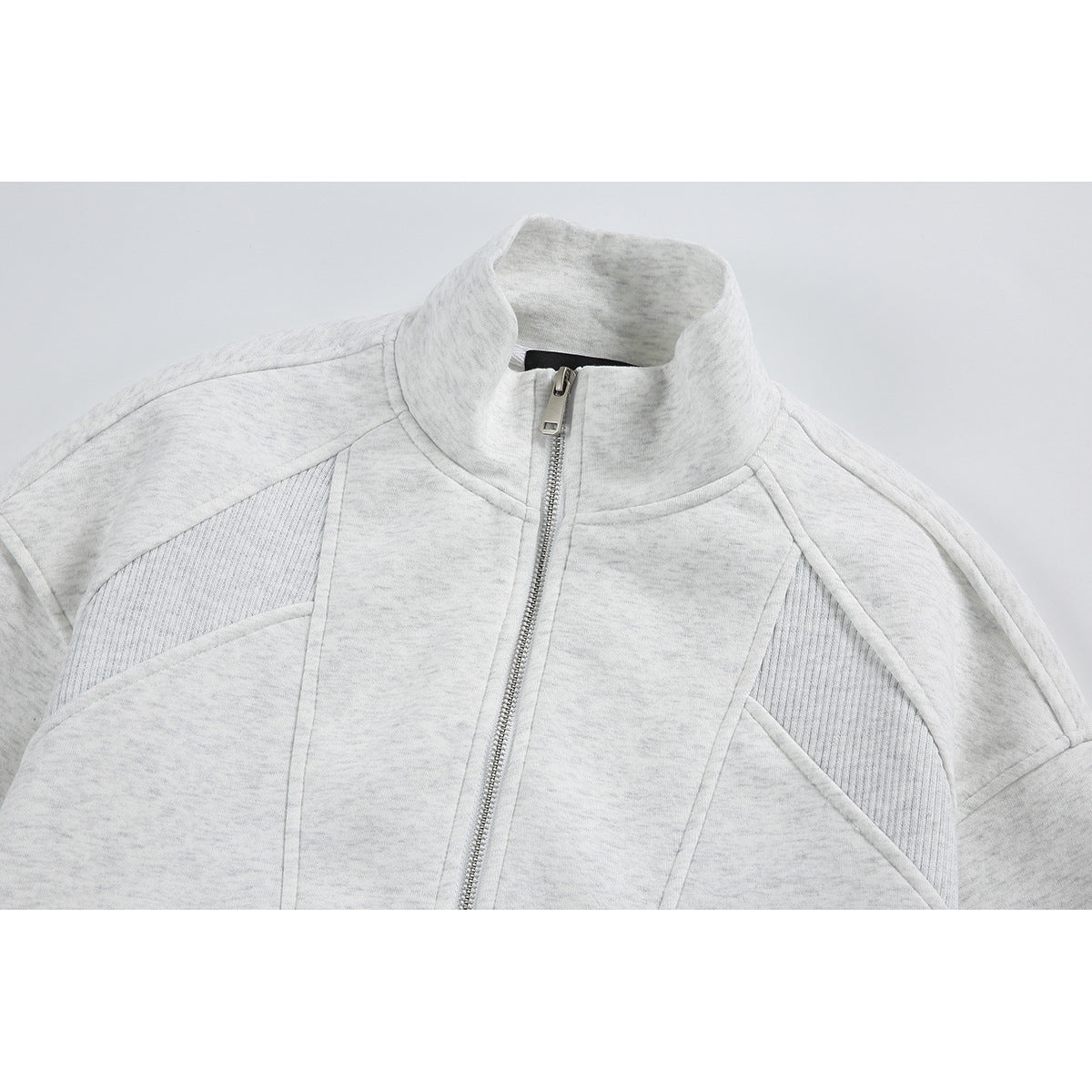 Close-up of a light gray zip-up jacket showing its stand collar, front zipper, and curved panel seams.