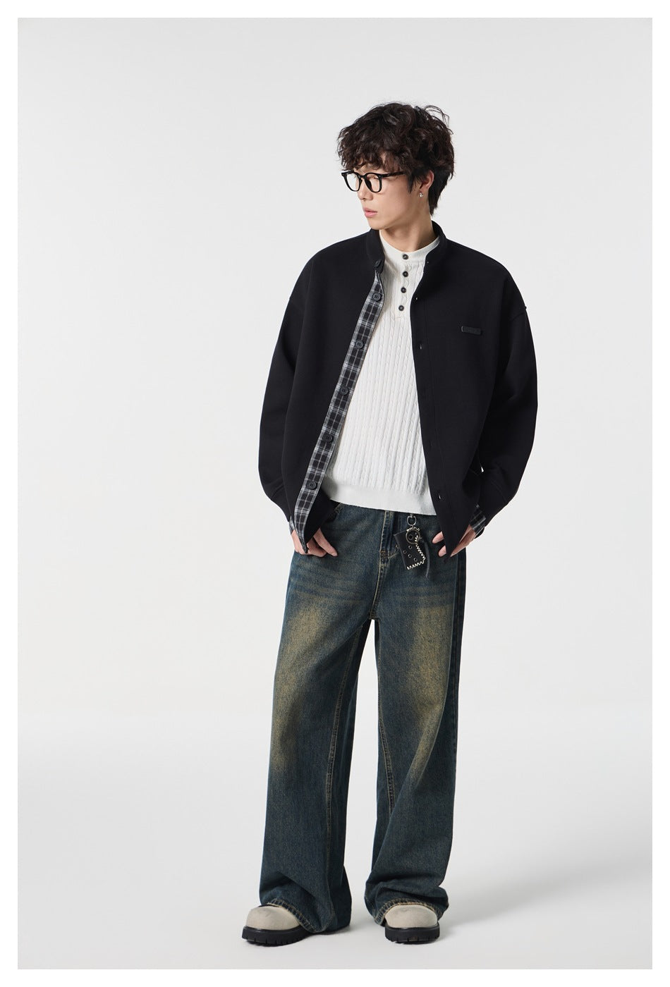 Model wearing the black stand-collar jacket open over a white sweater with wide-leg jeans, three-quarter side view