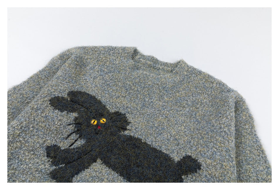 Close-up of a black cat motif with yellow eyes and a red nose on blue-gray marled sweater fabric.