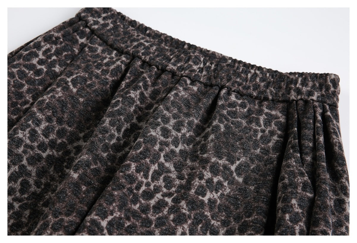 Close-up of the gathered waistband and pleated front of dark brown and black leopard-print trousers.