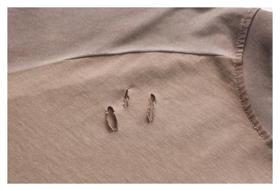 Close-up of three small distressed slits on taupe T-shirt fabric near a ribbed neckline.