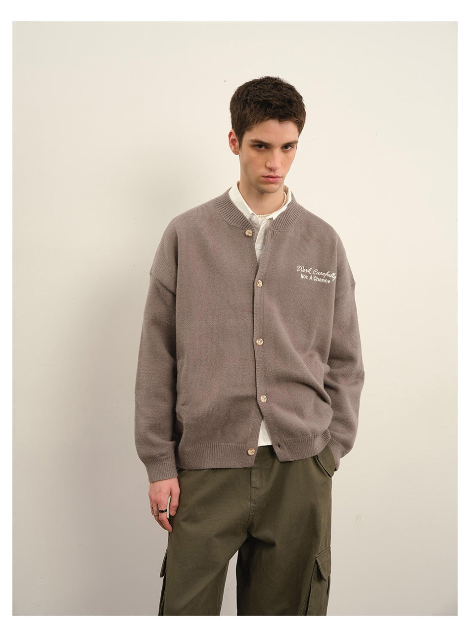 Close-up of a model wearing a taupe-gray knit cardigan with chest embroidery over a white shirt and olive cargo pants