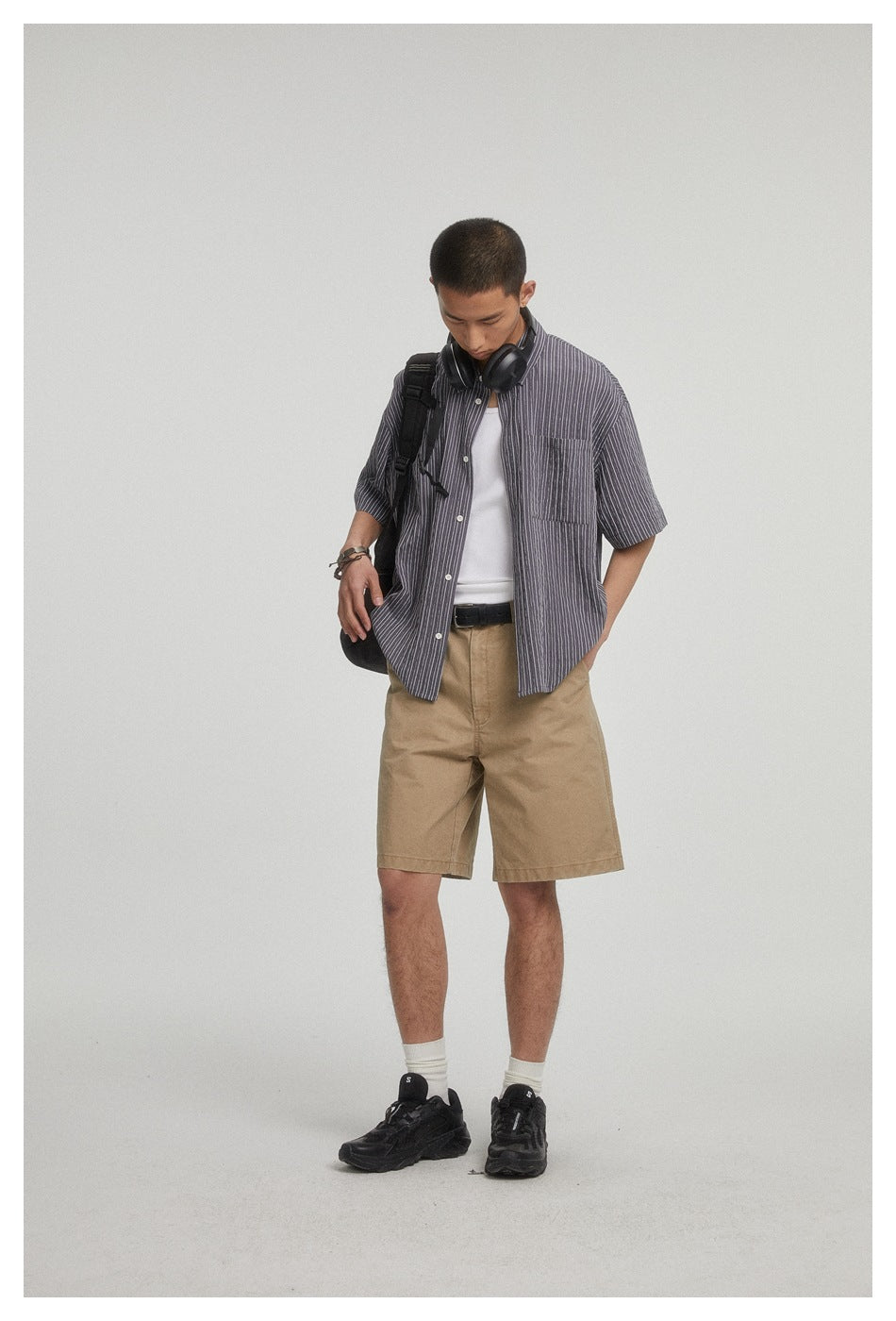 Model wearing a dark gray pinstriped short-sleeve button-up over a white top with tan shorts.