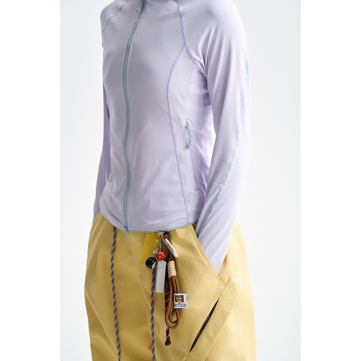 Close front view of a pale lilac ribbed zip jacket with aqua piping, worn with yellow trousers.