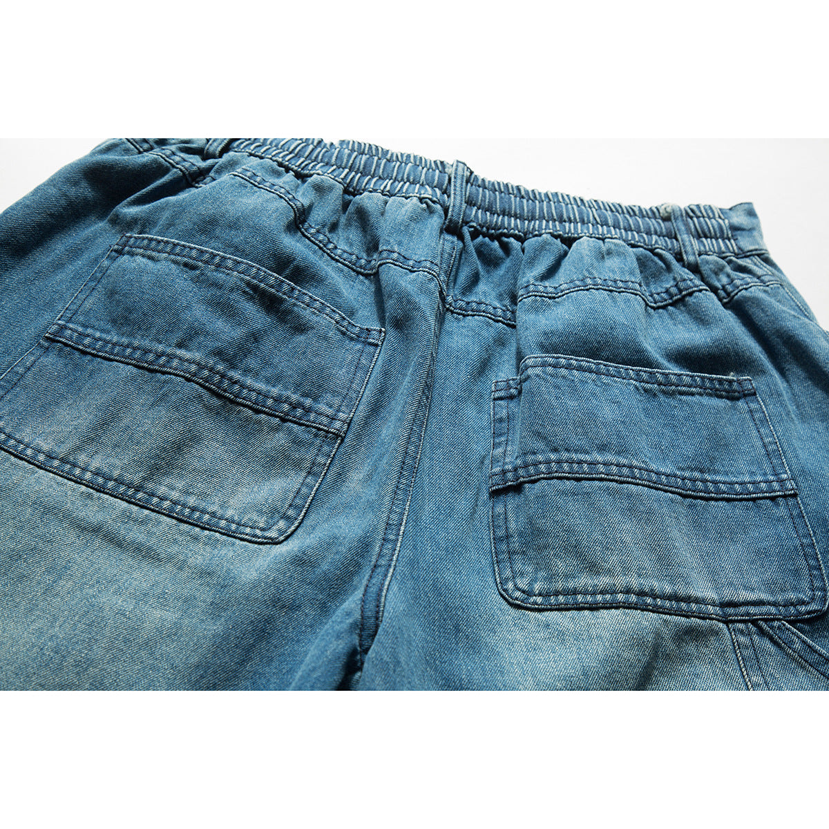 Close-up of the back of blue denim shorts, showing an elastic waistband and two patch pockets.