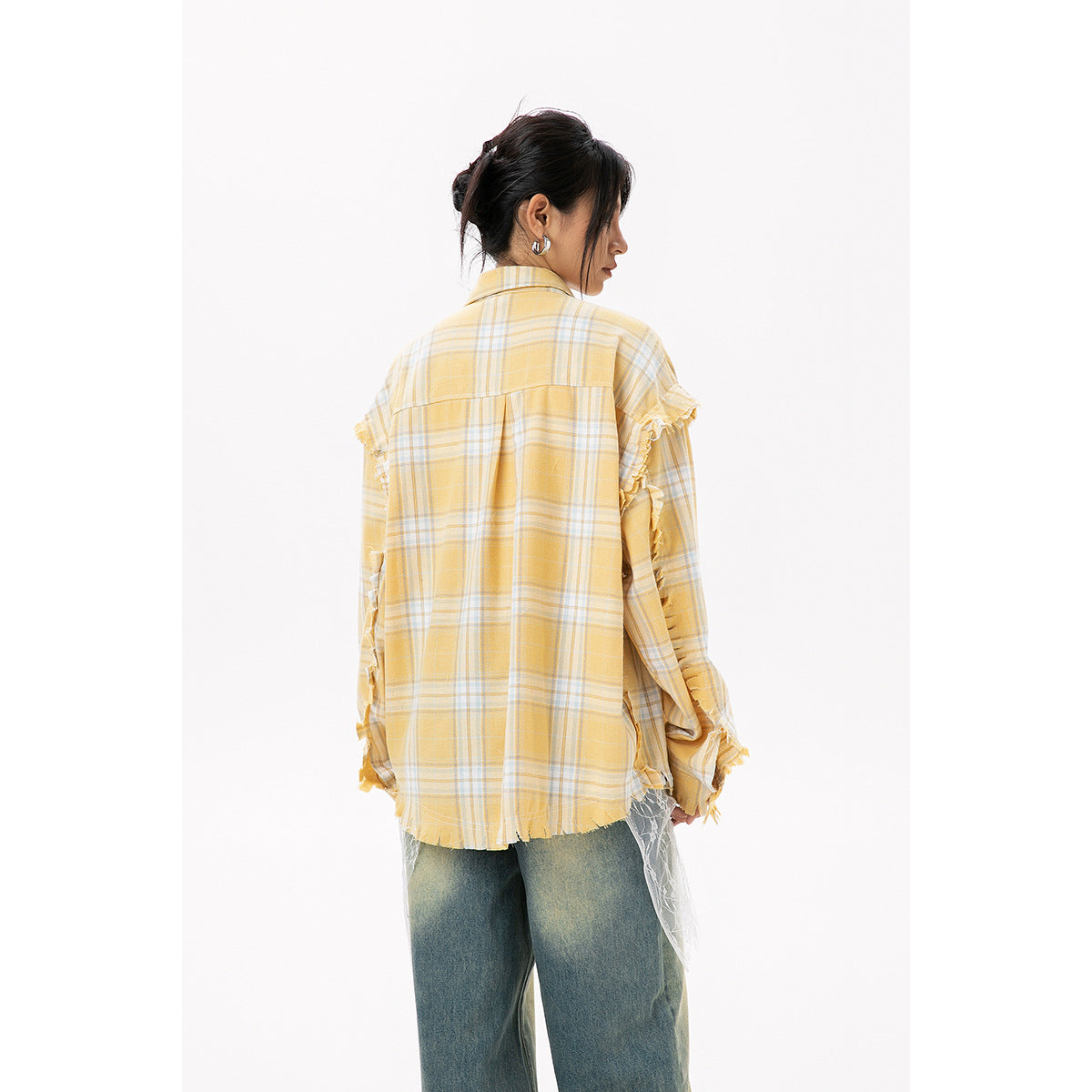 Rear view of a model wearing an oversized yellow plaid shirt with frayed sleeve and hem details, over wide-leg jeans.
