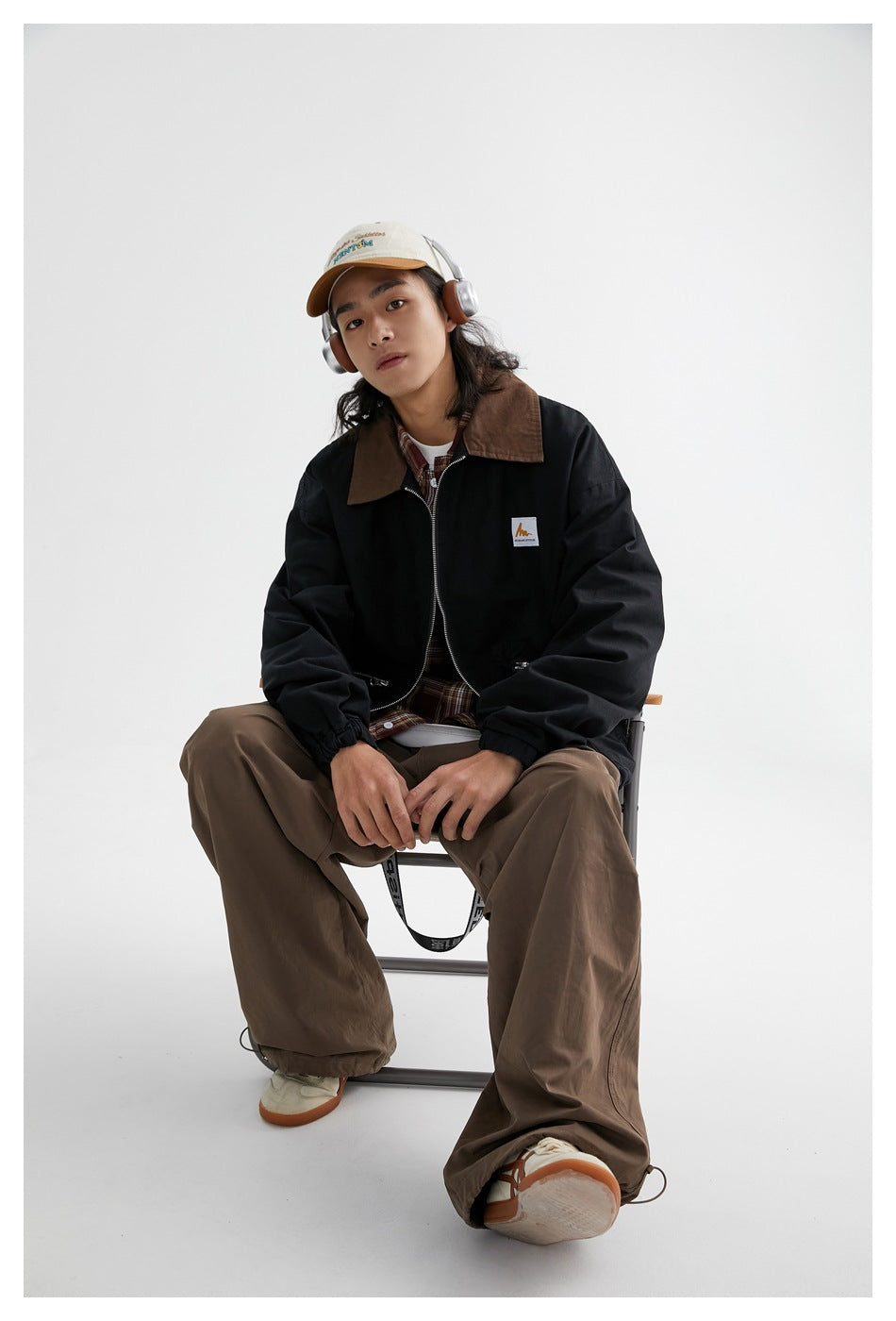 Seated model wearing a black zip jacket with a brown collar, zip pockets and gathered cuffs.