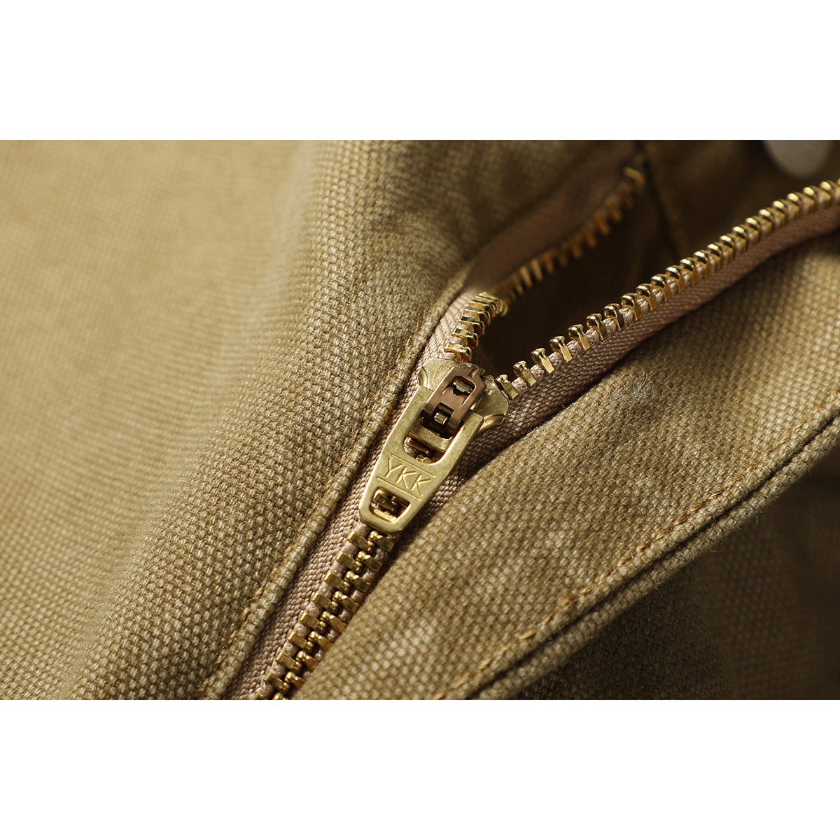 Close-up of a metal zipper and zipper pull on tan woven fabric.