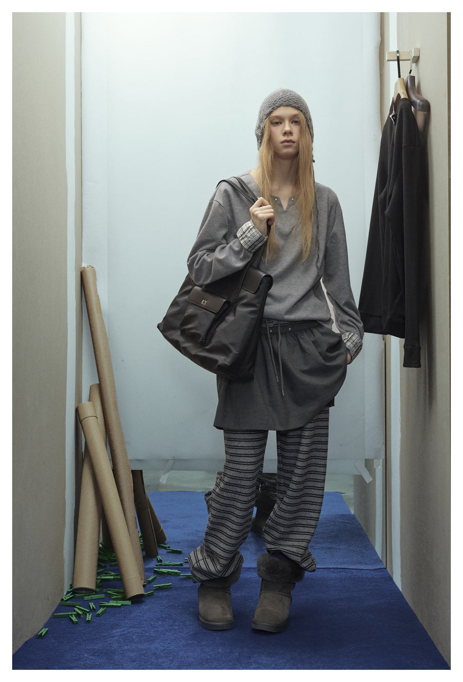 Model wearing gray V-notch top with plaid cuffs, layered over a gray skirt with a beanie and tote bag
