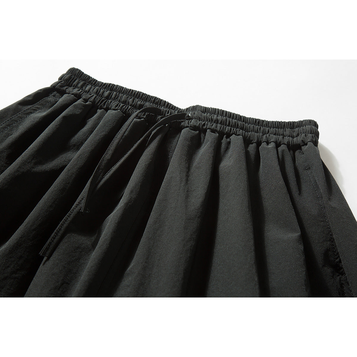 Close-up of black gathered elastic waistband with a drawstring and softly pleated fabric.