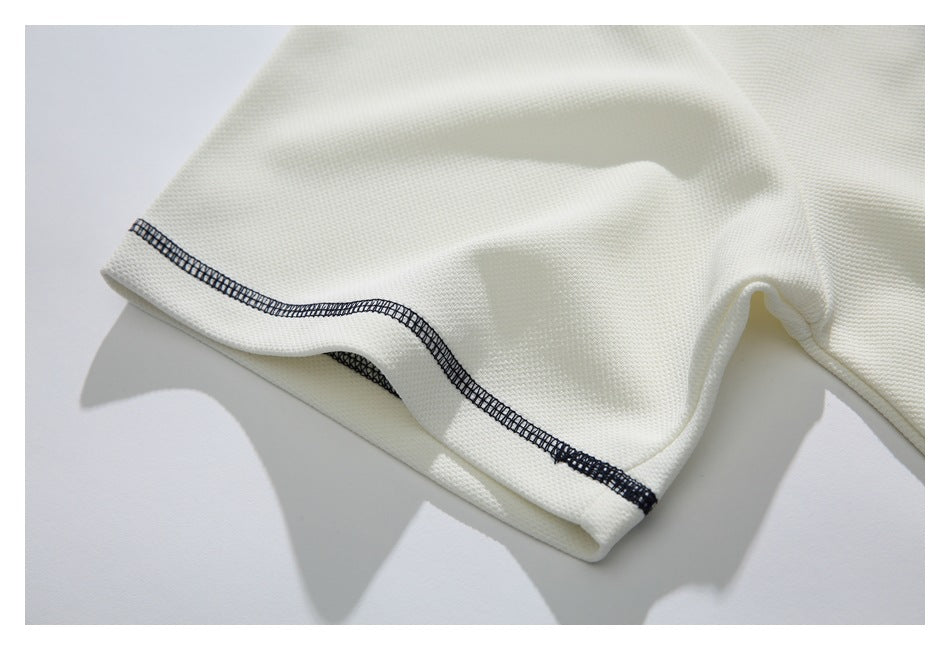 Close-up of an ivory shirt sleeve hem with dark navy decorative stitching.
