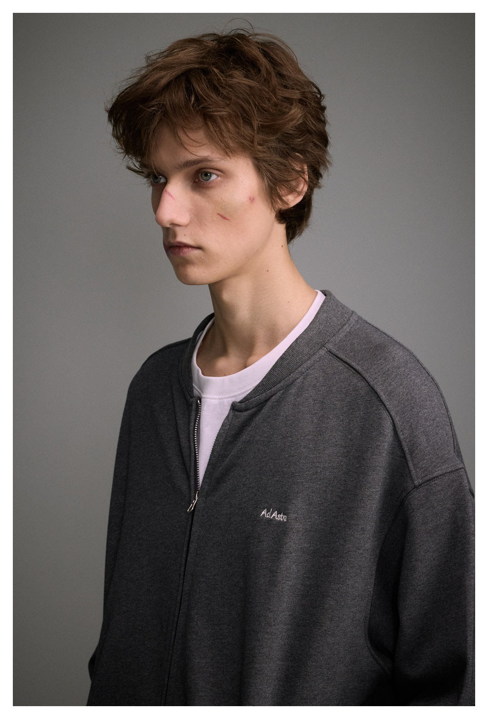 Close-up of a model wearing a charcoal gray zip-up jacket with a small embroidered chest logo.