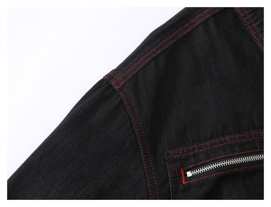 Close-up of a black denim jacket shoulder seam and silver zipper pocket with red stitching.