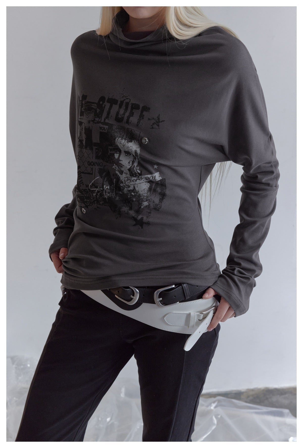 Close view of a model wearing a charcoal draped-neck long-sleeve top with a dark graphic print and metal snaps.