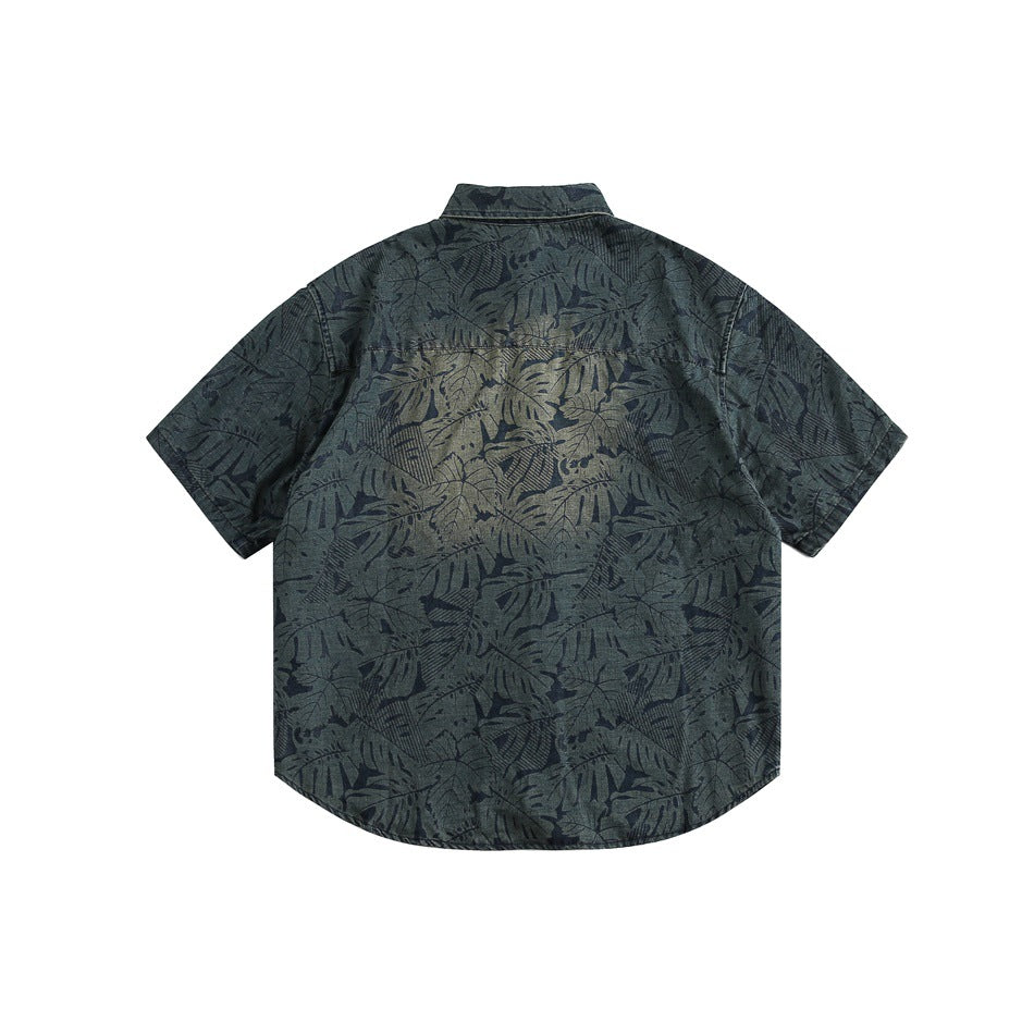 Back view of a dark blue-green short-sleeve shirt with an allover leaf print and curved hem.