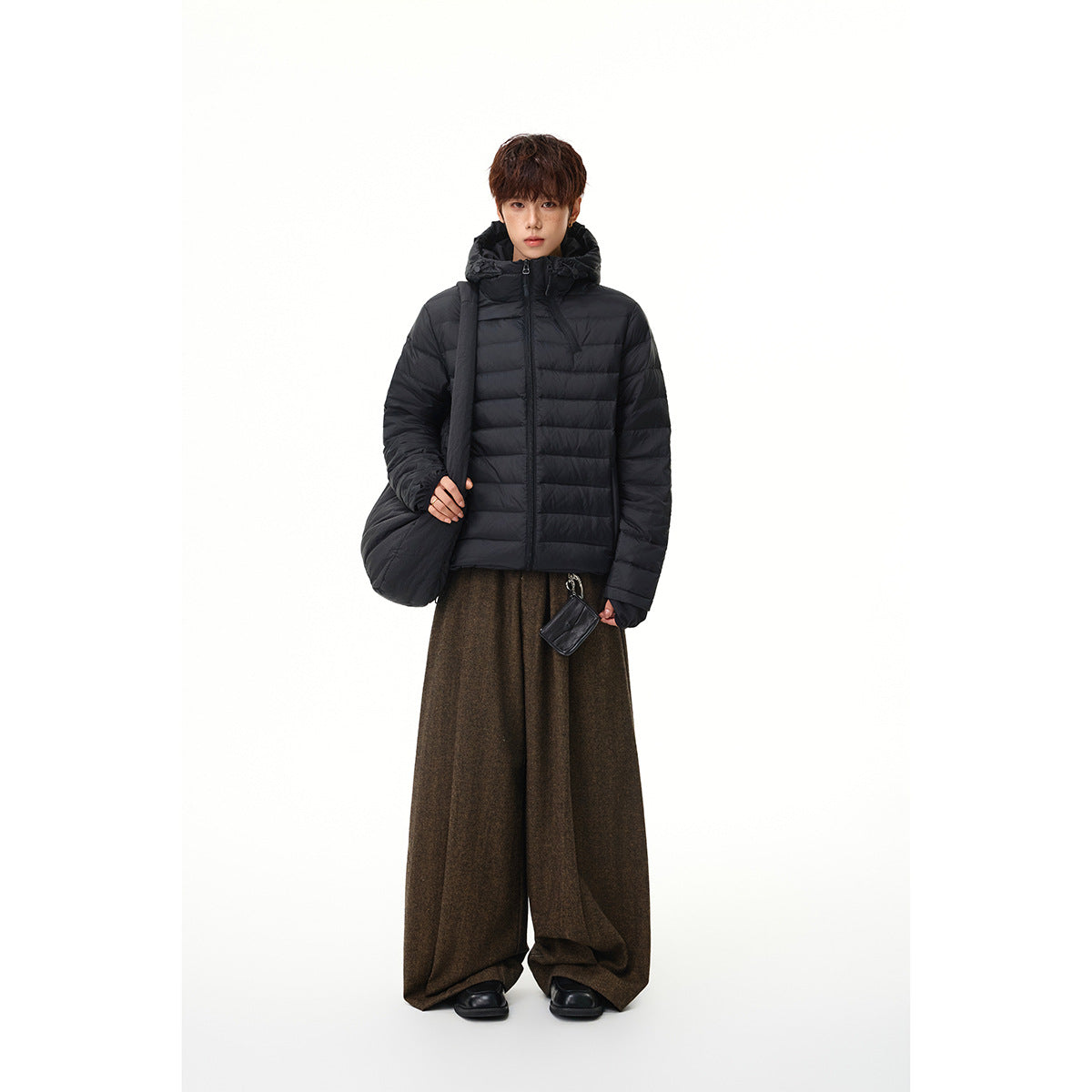 Full-length model wearing a black hooded puffer jacket with loose brown trousers.
