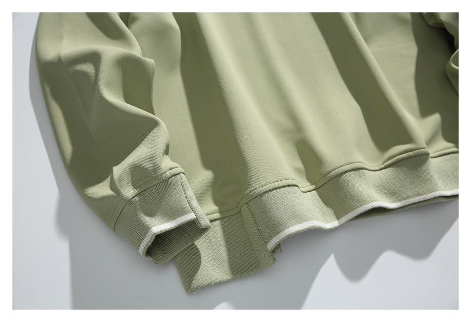 Close-up of the sage-green sweatshirt’s ribbed hem and cuff, each edged with a narrow white stripe.