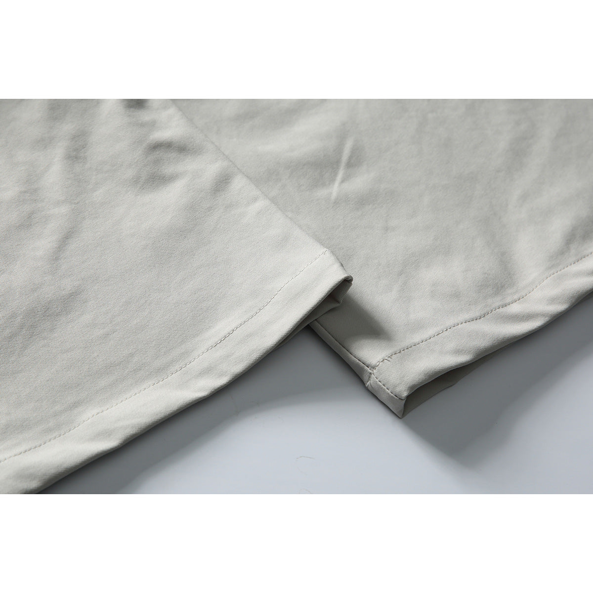 Close-up of the stitched hems on light gray trouser legs.