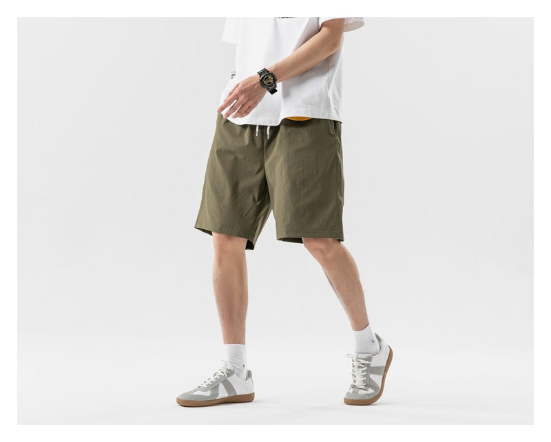 A model wearing olive green drawstring shorts and a white T-shirt, shown in a walking pose.