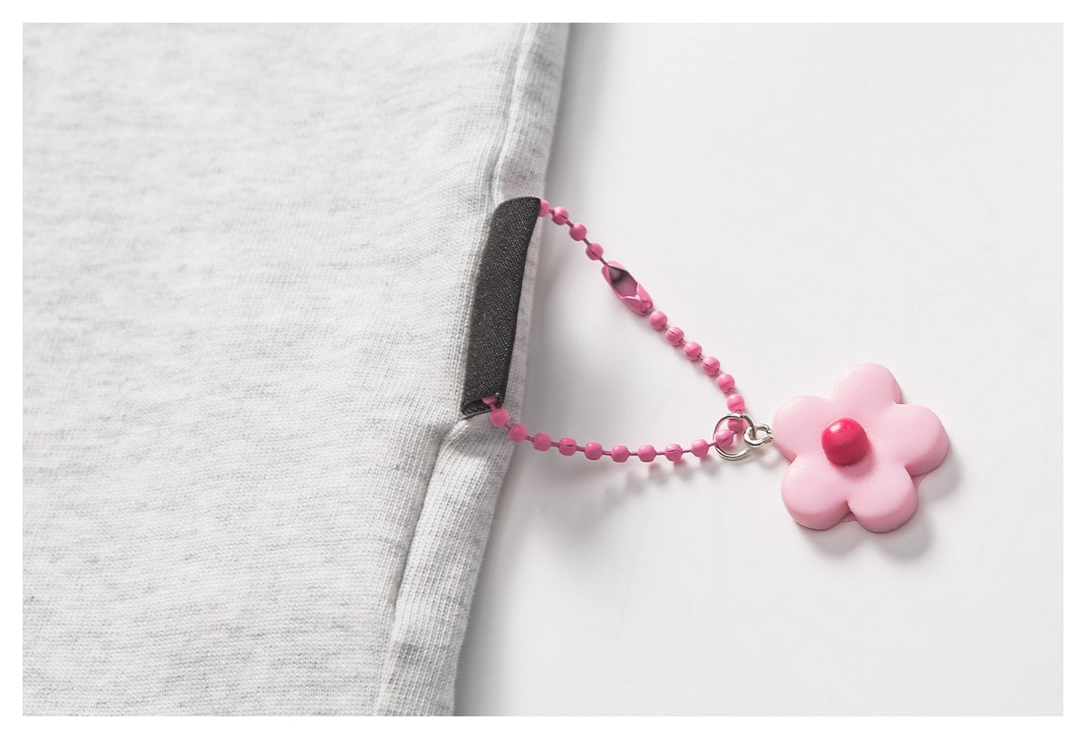 Close-up of a light gray shirt side seam with a small black tab and dangling pink flower charm.