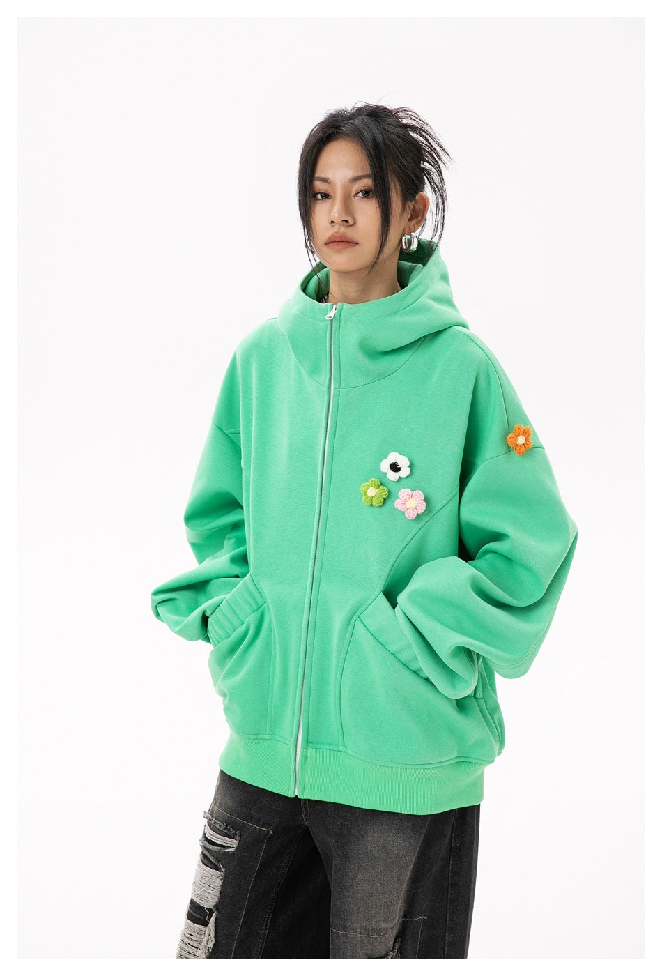 Model wearing a zipped mint-green hoodie with large front pockets and colorful flower appliqués on the chest and sleeve.