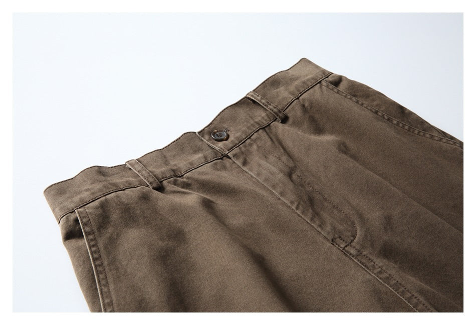 Angled flat lay of brown trousers showing the waistband, button, belt loops, front pocket, and fly.