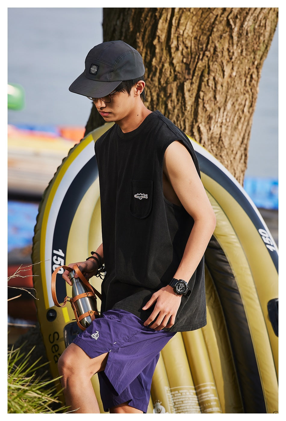Model wearing a loose black sleeveless pocket shirt and purple shorts, shown from the side.