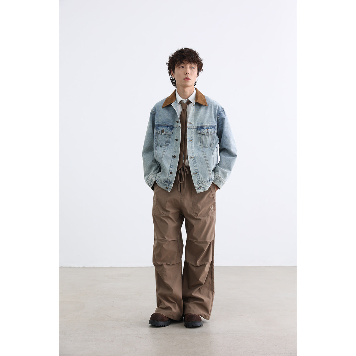 Model wearing a light-wash denim jacket with a brown collar and roomy brown trousers, shown full length from the front.