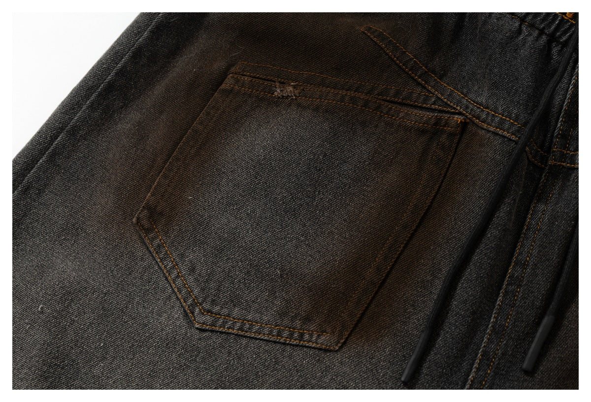 Close-up of a charcoal denim pants pocket, waistband, and black drawstring with ochre stitching.