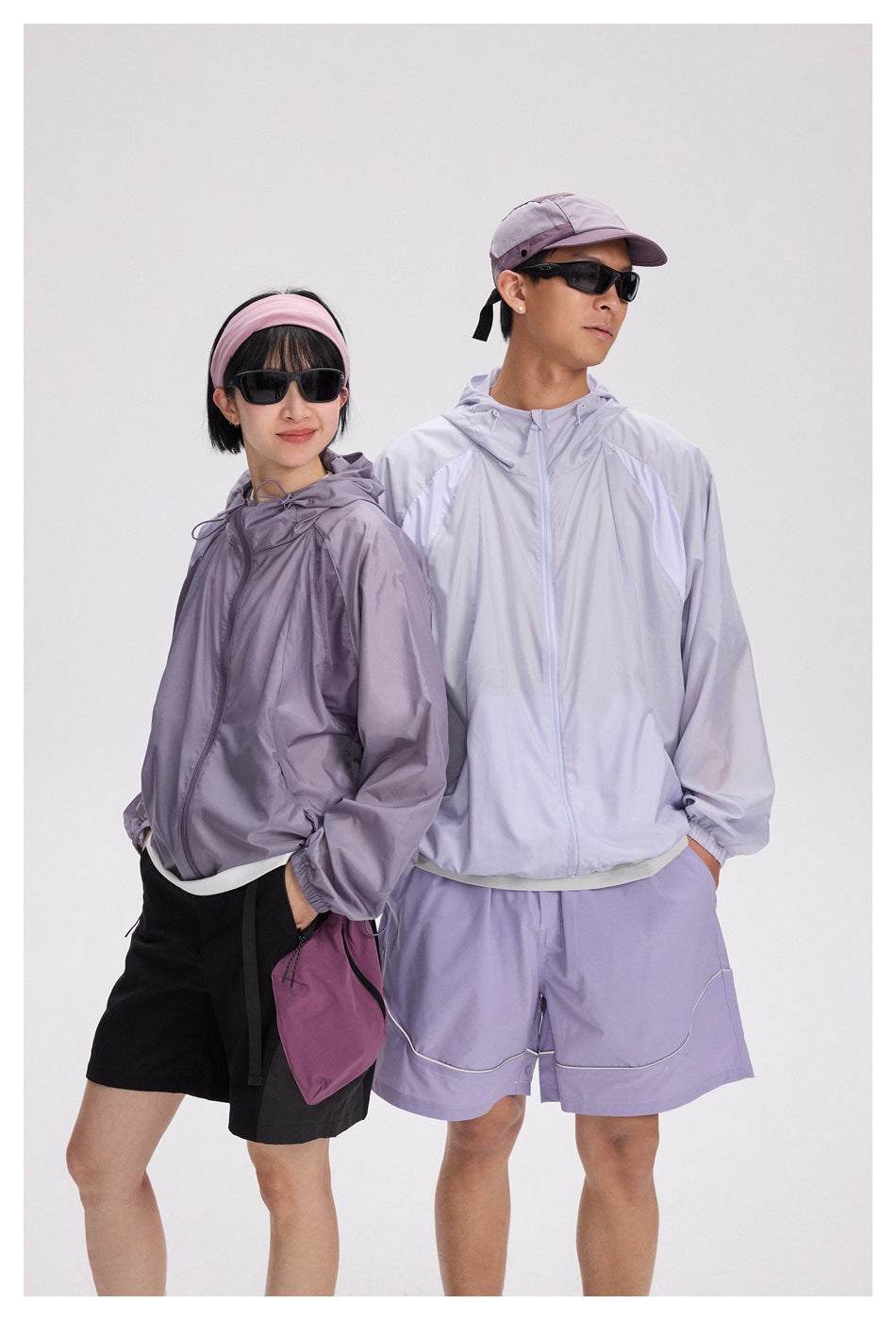 Two models pose in lavender hooded jackets, with the woman in black shorts and the man in lavender shorts.