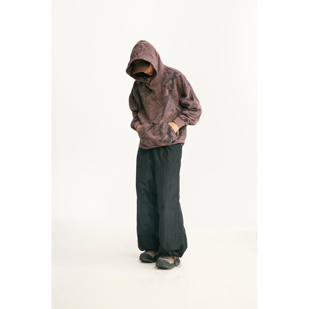 Model wearing a mauve patterned hooded pullover and loose black pants.