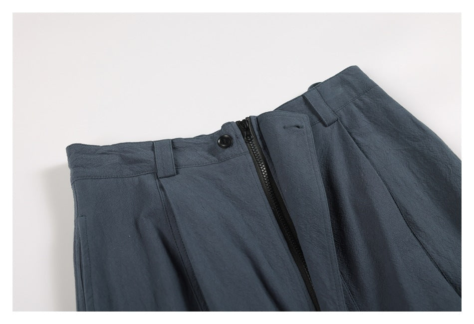 Close-up of blue-gray trousers showing the waistband, belt loops, button, and front zipper.