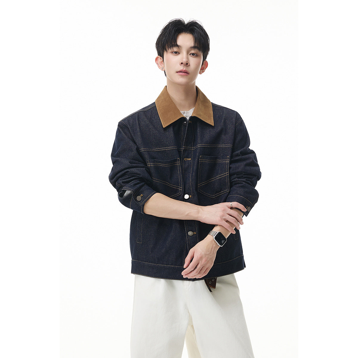 Model wearing a dark indigo denim jacket with a tan collar and contrast stitching, paired with white trousers.