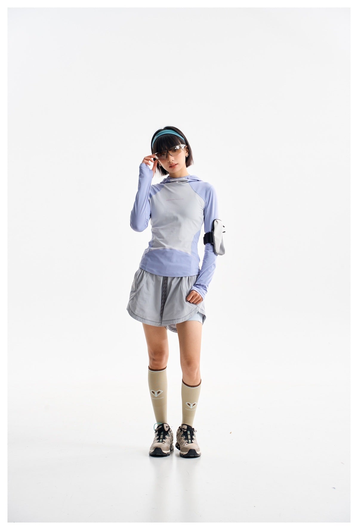Model in a lavender and light gray hooded top and gray running shorts, posing in sunglasses and knee-high socks.