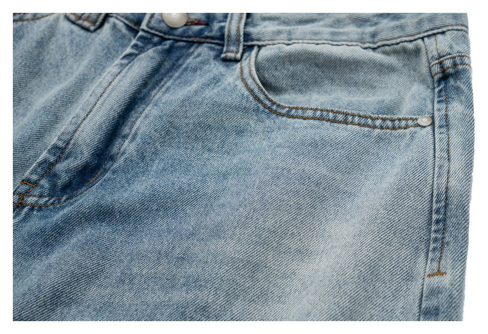 Close-up of light blue jeans showing the curved front pocket, rivet, waistband, and belt loop.